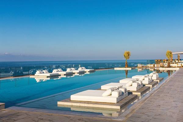 Außenpool des Abaton Island Resort mit Blick auf das Meer und weißen Sonnenliegen.