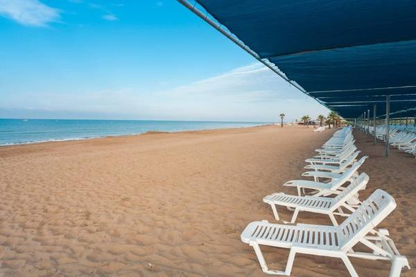 Strand des Club Grand Side Hotels mit weißen Sonnenliegen und blauem Sonnendach.