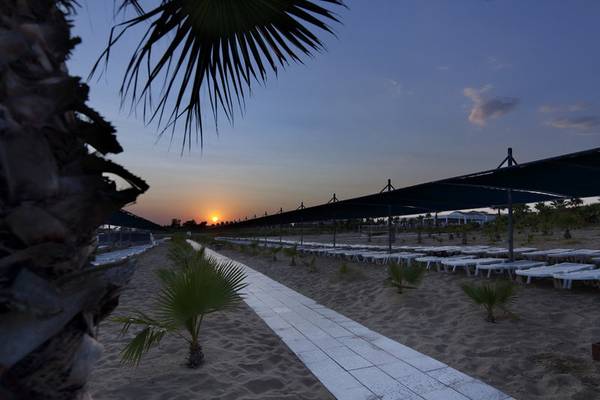 Sonnenuntergang am Strand des Club Grand Side Hotels mit weißen Liegestühlen und Palmen.