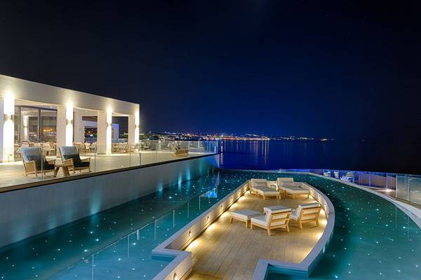 Nachtansicht des Abaton Island Resort & Spa mit beleuchtetem Infinity-Pool und Blick auf das Meer