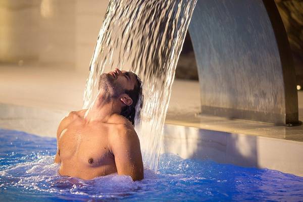 Mann genießt Wasserfall im Schwimmbad des Abaton Island Resort & Spa