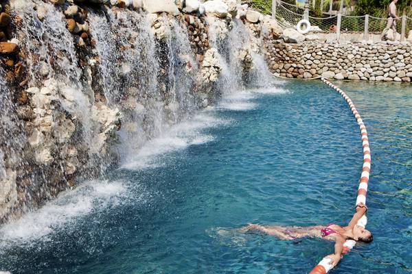 Eine Frau schwimmt im Pool mit einem Wasserfall im Hintergrund.