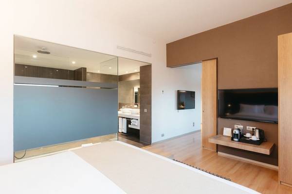 Innenansicht eines Hotelzimmers im Barcelo Valencia, mit Glaswand, Bad, Fernseher und Schreibtisch.