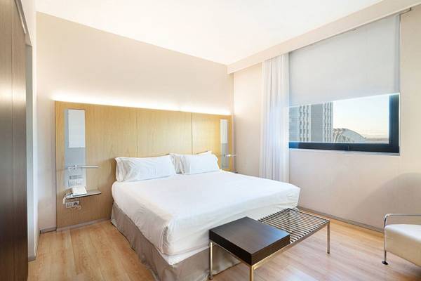 Das Barcelo Valencia Hotelzimmer mit einem großen Bett, weißen Kissen und einem Nachttisch.