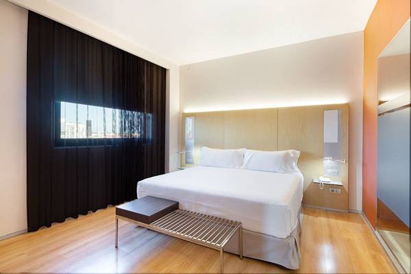 Ein modernes Hotelzimmer im Barcelo Valencia mit weißem Bett, Nachttisch und Holzboden.