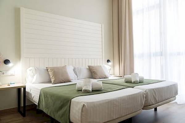 Zwei Betten im Hotelzimmer des DWO Valencia mit grünen Decken und weißen Kissen.