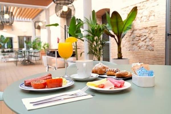 Frühstückstisch im Hotel DWO Valencia mit Orangensaft, Croissants, Wurst und Tomaten.
