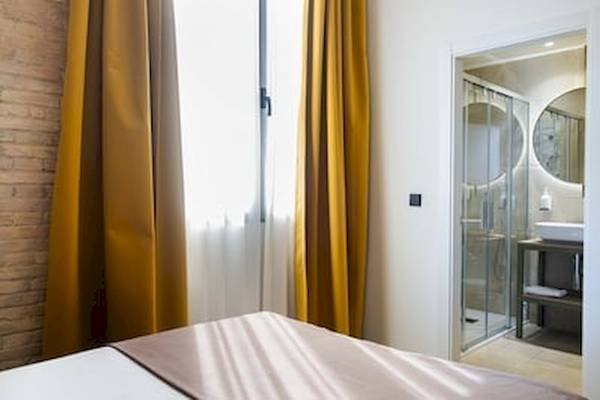 Innenansicht eines Zimmers im DWO Valencia Hotel mit Bett, gelben Vorhängen und Glasdusche.
