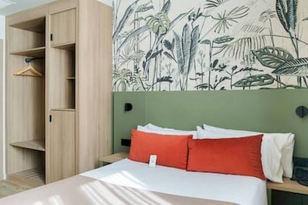 Schlafzimmer im DWO Valencia Hotel mit grüner Wand, Pflanzentapete, Bett, roten Kissen und Kleiderschrank.