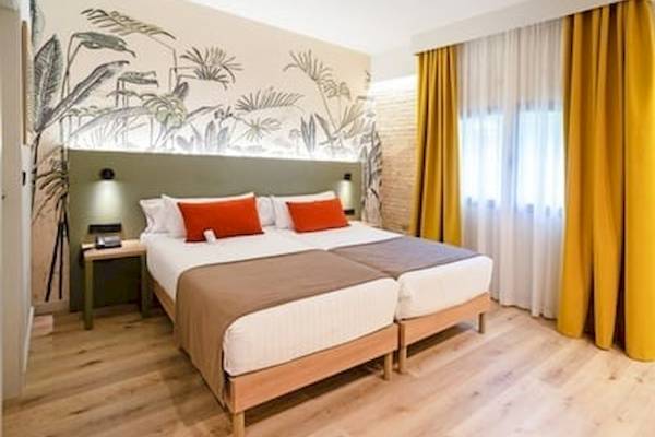 Schlafzimmer im DWO Valencia mit zwei Betten, grüner Kopfteilwand, Pflanzentapete und gelben Vorhängen.