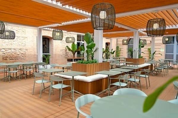 Außenbereich des DWO Valencia Hotels mit runden Tischen und Stühlen unter einer Holzüberdachung.