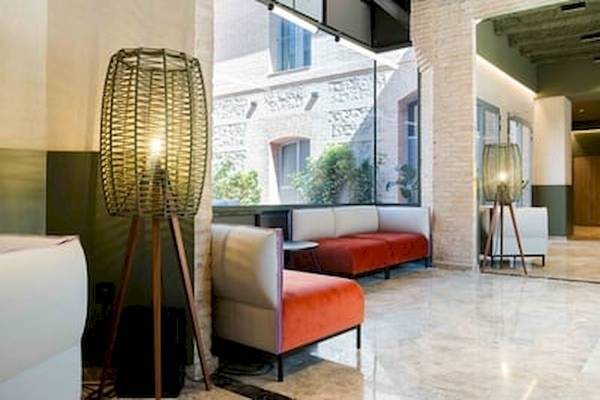 Hotellobby des DWO Valencia mit weißen Möbeln, orangefarbenem Sofa und großen Fenstern.