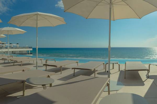 Terrasse des RH Bayren & Spa Hotels mit weißen Sonnenliegen und Sonnenschirmen am Meer