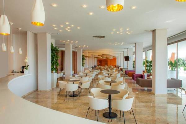 Innenbereich des RH Bayren & Spa Hotels mit vielen Tischen und Stühlen, Pflanzen und hängenden Lampen.