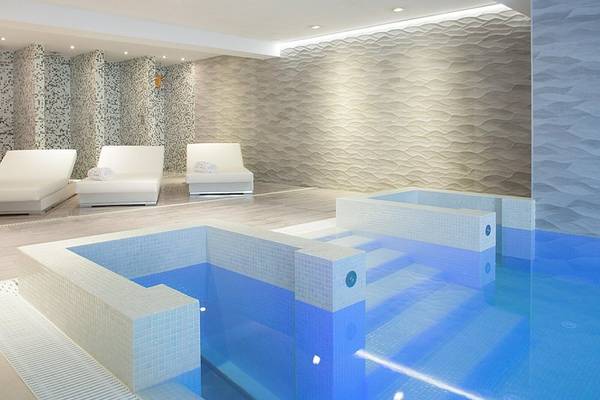 Innenpoolbereich des RH Bayren & Spa mit Lounge-Bereich und weißen Liegen.
