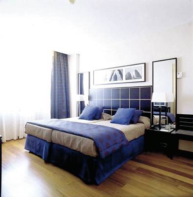 Doppelbett-Zimmer im Eurostars Grand Valencia mit blauen Kissen und Decken, weiße Wände und Holzboden.