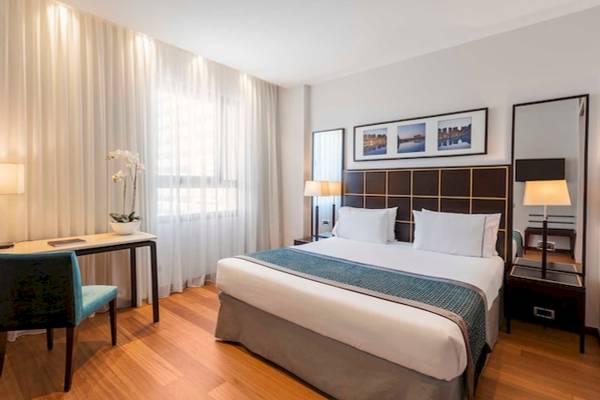 Ein elegantes Hotelzimmer im Eurostars Grand Valencia mit Doppelbett, Schreibtisch, Blumen, und großen Fenstern.