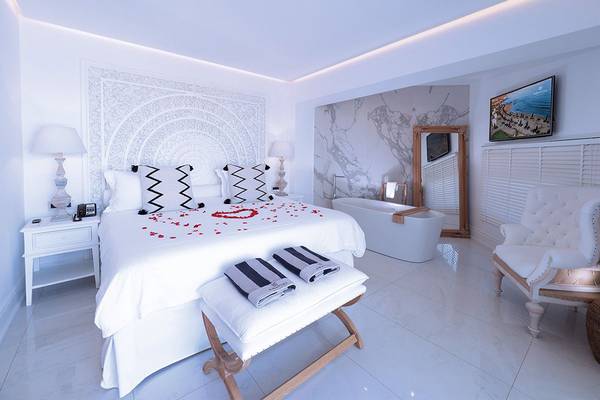 Schlafzimmer im Abaton Island Resort & Spa mit weißem Bett, Badewanne, Spiegel und Rosenblättern.