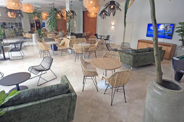 Lounge Bereich im Hotel Principal Affiliated by RH mit vielen Stühlen und Tischen, Pflanzen und einer Fernsehwand.