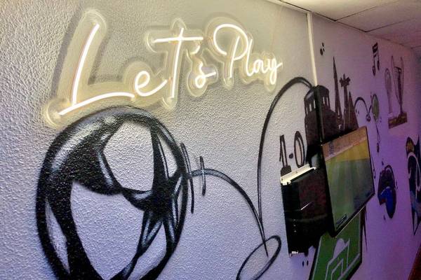 Eine Wand mit Graffiti, einem Fußball und der Beschriftung 'Let's Play'.