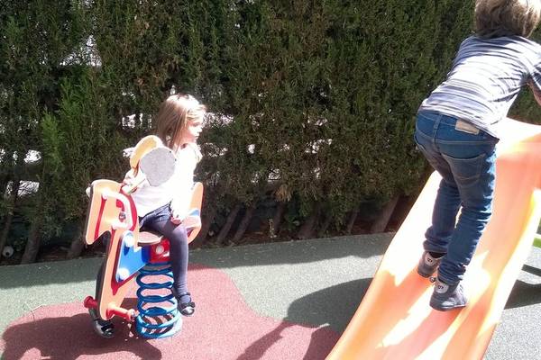 Zwei Kinder spielen auf einem Spielplatz, eines auf einem Pferdchen und das andere auf einer Rutsche.