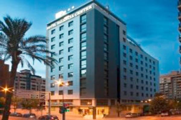 Außenansicht des Valencia Center Hotels mit Palme und Stadtbeleuchtung im Hintergrund.