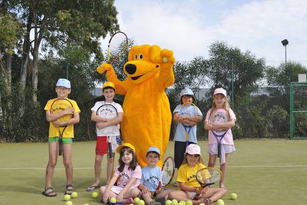 Kinder posieren mit Tennisschlägern und einem Maskottchen auf einem Tennisplatz im Almar Timi Ama Resort & Spa