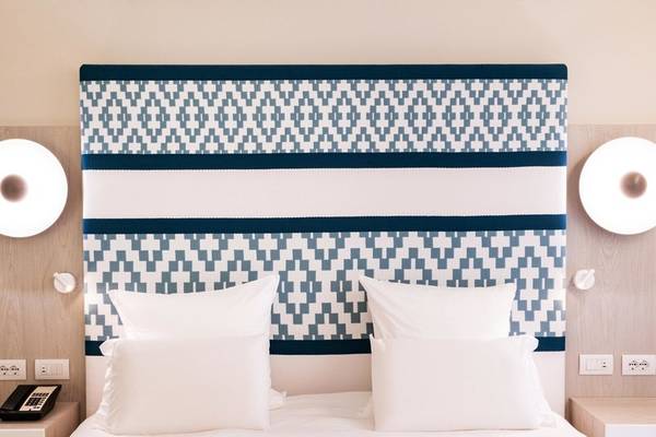 Hotelzimmerbett mit weißem Bettlaken, weißen Kissen und blau-weißem Kopfteil.