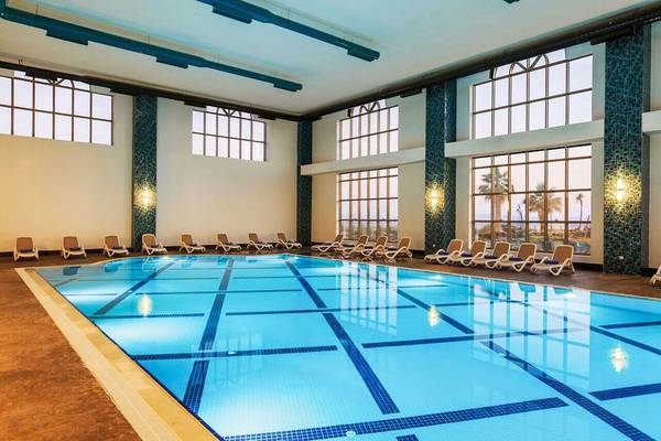 Ein großer Innenpool im Sunis Efes Royal Palace Resort & Spa mit Liegestühlen und großen Fenstern.
