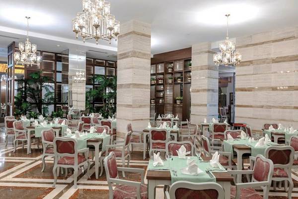 Das elegante Restaurant des Sunis Efes Royal Palace Resort & Spa mit grün gedeckten Tischen und hängenden Kronleuchtern.