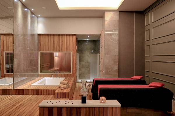 Innenansicht eines Spa-Bereichs mit Badewanne, zwei Liegen und Holzboden.