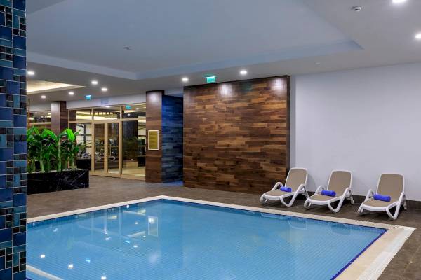 Innenpool des Sunis Efes Royal Palace Resort & Spa mit drei Liegestühlen und blauen Handtüchern.