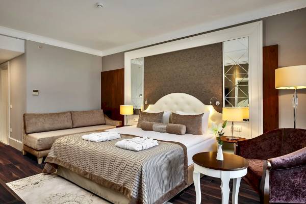 Elegant Hotelzimmer im Sunis Efes Royal Palace Resort & Spa mit Kingsize-Bett, Sofa, Tisch und Nachttischen.