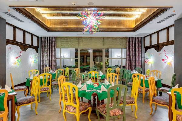Innenbereich des Restaurants im Sunis Efes Royal Palace Resort & Spa mit farbigen Stühlen und grünen Tischen.