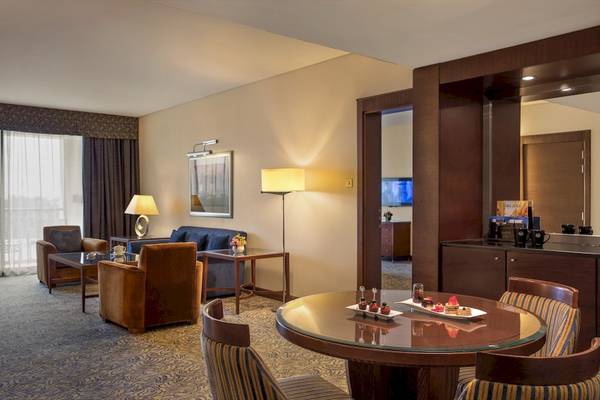 Innenansicht einer Hotelsuite im Al Ain Rotana mit Wohnzimmer, Couch, Tisch und Fernseher.