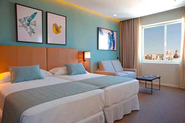 Innenansicht eines Doppelzimmers im Riu Plaza Espana Hotel mit zwei Betten, einem Sofa und einem Fenster.