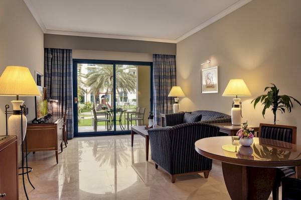 Wohnbereich des Al Ain Rotana Hotels mit großem Fenster und Blick auf Palmen.