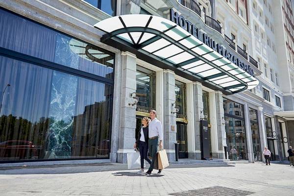 Zwei Leute gehen vor dem Riu Plaza Espana Hotel, mit Einkaufstüten in der Hand.