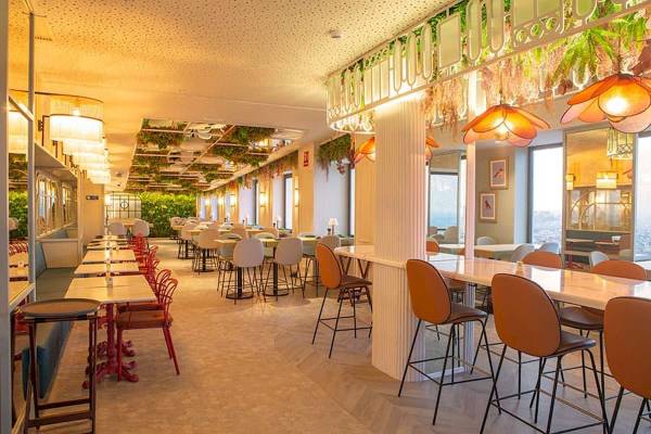 Innenbereich des Riu Plaza Espana Restaurants mit Tischen, Stühlen und grünen Pflanzen an der Decke.