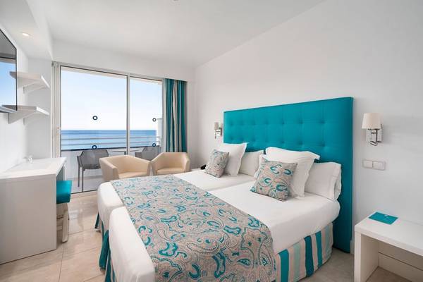 Hotelzimmer mit Meerblick im ALUA Gran Camp de Mar mit zwei Betten, blauem Kopfteil und Blick auf den Ozean.