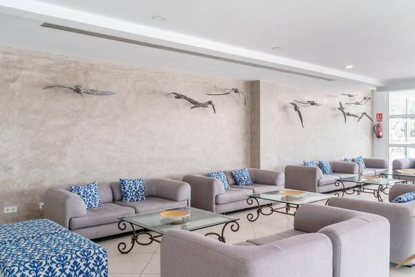 Lobby des ALUA Gran Camp de Mar Hotels mit grauen Sofas, blauen Kissen und Glastischen.