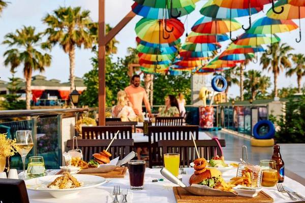 Terrasse im Magic Life Jacaranda Hotel mit bunten Regenschirmen, bunten Tischen und Stühlen, Essen und Getränken.