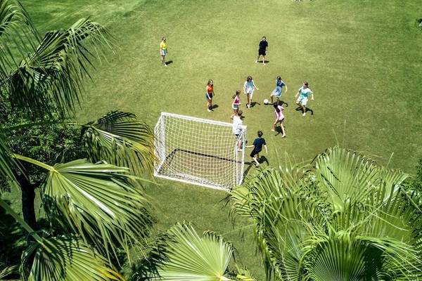 Kinder spielen Fußball auf einem grünen Rasenfeld im Magic Life Jacaranda Hotel.