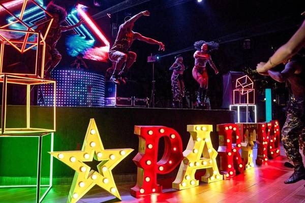 Party auf der Bühne im Magic Life Jacaranda Hotel mit leuchtenden Neon-Lettern und tanzenden Gästen.