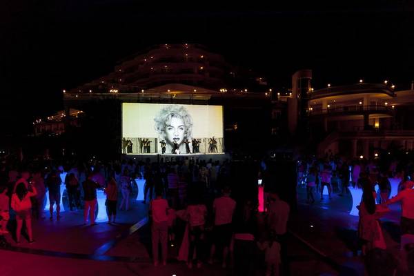 Abendveranstaltung im Starlight Resort Hotel mit einer großen Leinwand, auf der ein Foto von Madonna und einer Tanzgruppe zu sehen ist.