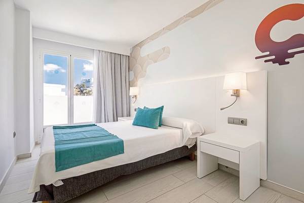 Ein modernes Zimmer im Calimera Balansat Resort mit weißem Bett, blauer Decke und grünen Kissen.