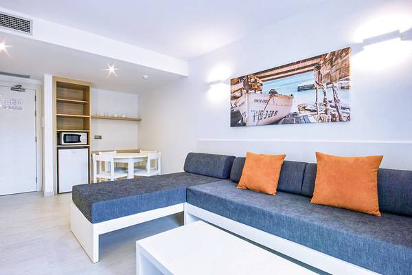 Innenraum des Calimera Balansat Resorts mit einem L-förmigen Sofa, Kissen, Tisch und Mikrowelle.