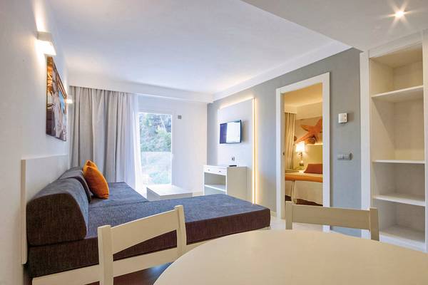 Innenansicht eines Zimmers im Calimera Balansat Resort mit Schlafsofa, Tisch und Fernseher.