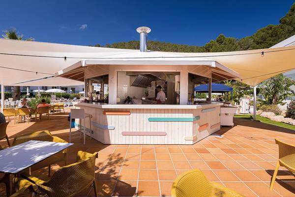 Terrasse des Calimera Balansat Resorts mit bunten Bänken und einem Mitarbeiter hinter dem Tresen.