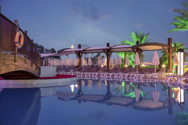 Poolbereich im Granada Luxury Okurcalar Hotel bei Nacht mit Sonnenliegen und Schirmen.